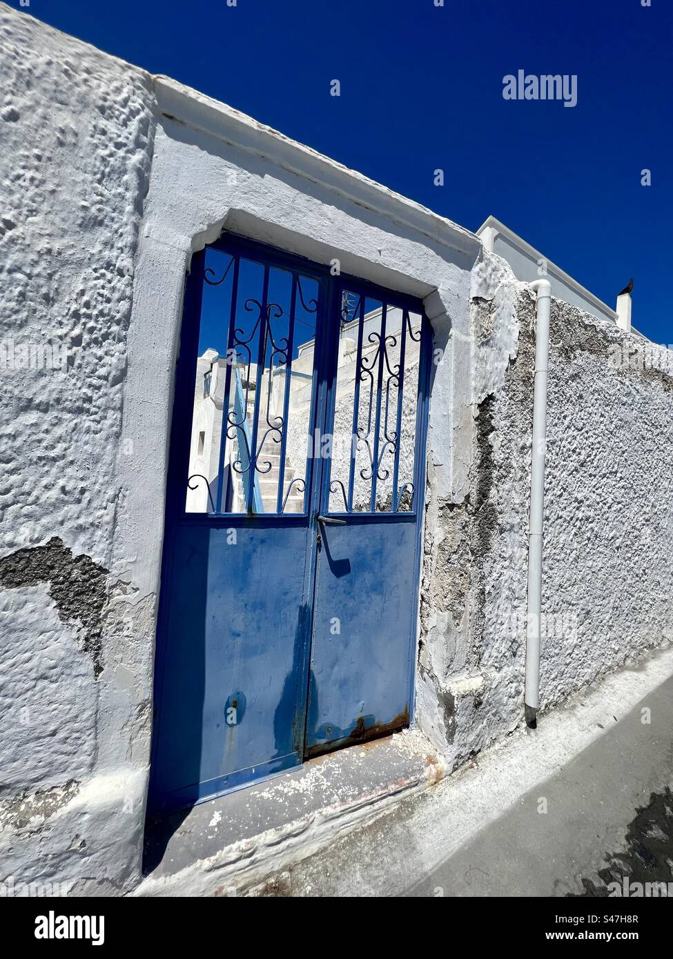 Typical Santorini blue gated entrance surrounded by whitewashed volcanic rock architecture under a clear blue summer sky. - Smartphone Captured Stock Image
