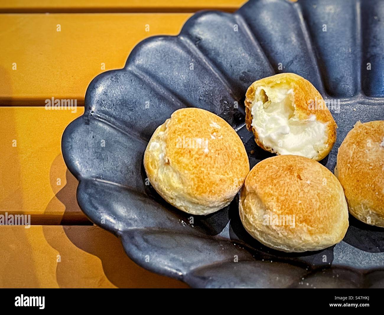 High angle view of mini vanilla cream puffs in black bowl on yellow wooden table. - Smartphone Captured Stock Image