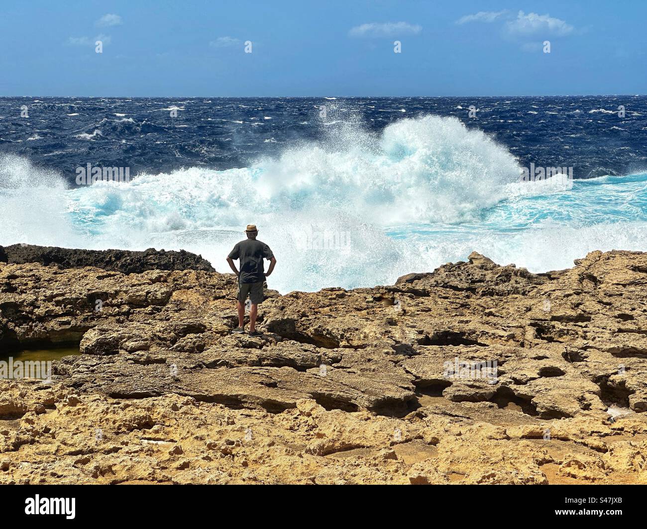 Person standing on rocks watching breaking waves at St Lawrence on the coast of the island of Gozo - Smartphone Captured Stock Image
