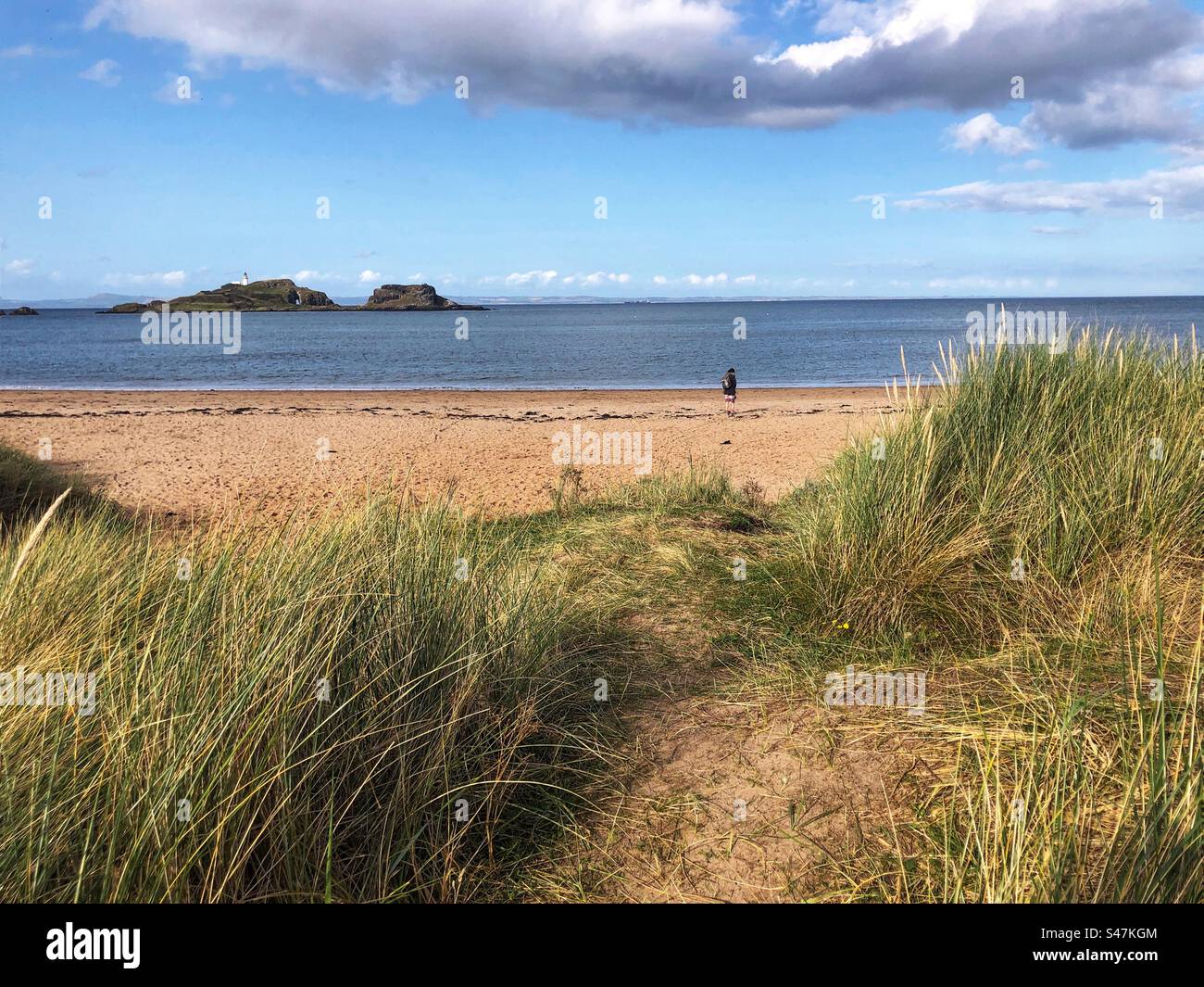 Solitary Walker on Yellowcraig beach, with a view towards Fidra lighthouse, East Lothian coast, Scotland - Smartphone Captured Stock Image