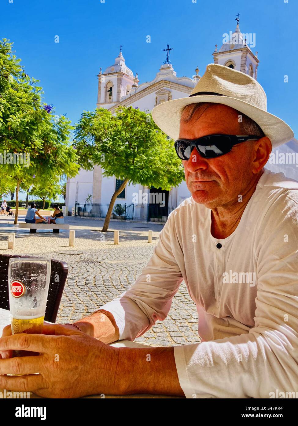 Man with sunglasses and Fedora hat relaxing with a beer in the old town square of Lagos Portugal in the Algarve - Smartphone Captured Stock Image