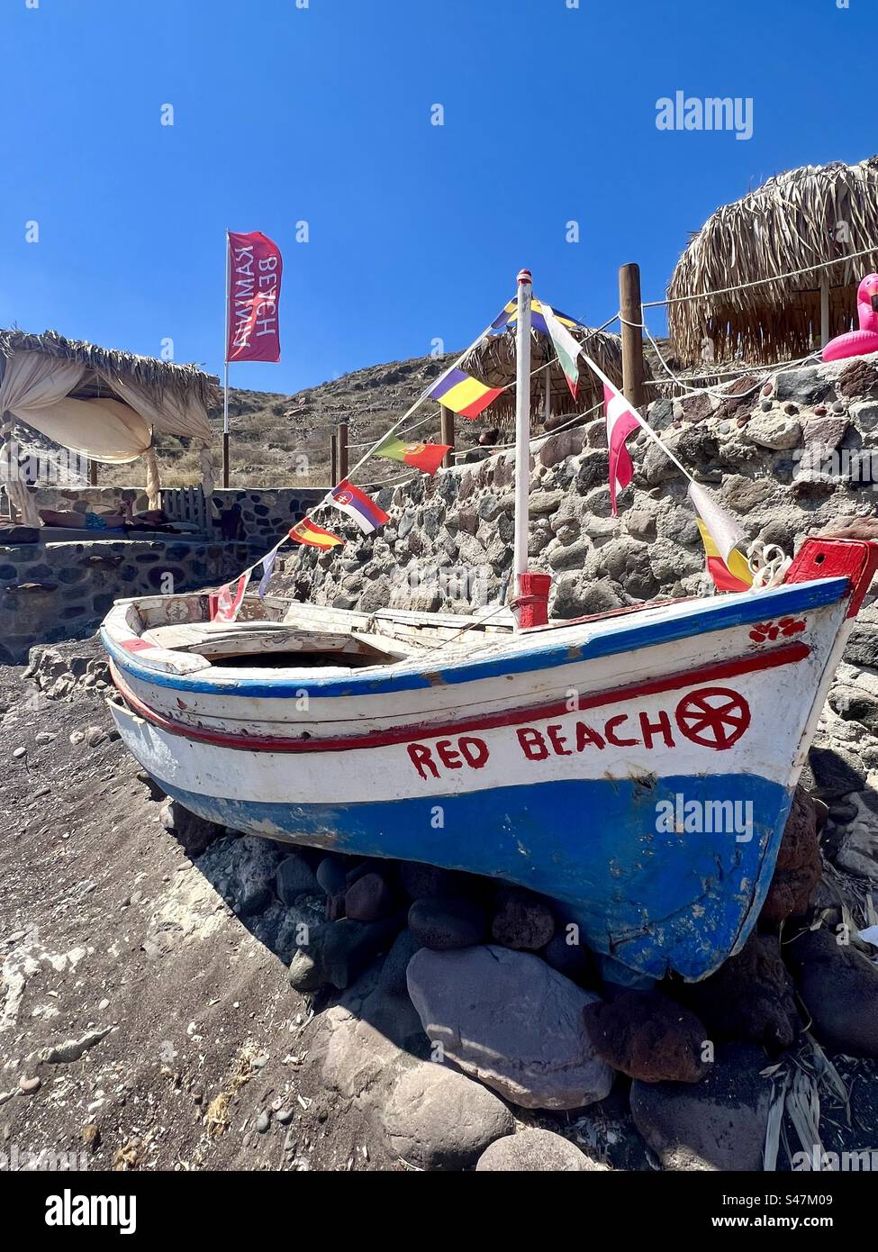A painted old boat on the sand and rocks of Kaminia Beach next to Red Beach on Santorini island - Smartphone Captured Stock Image