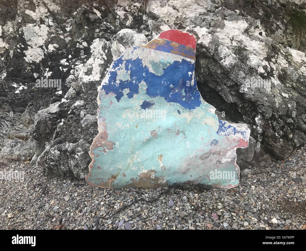 Fibreglass section of boat against very old rocks on beach - Smartphone Captured Stock Image