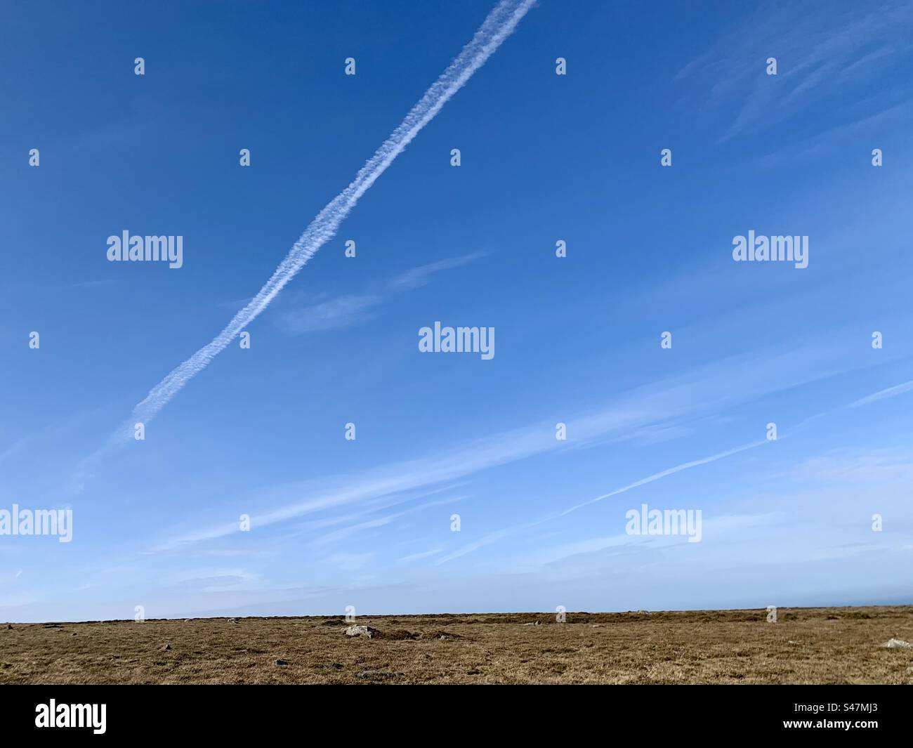 Big blue sky with white aeroplane contrail lines above barren landscape - Smartphone Captured Stock Image
