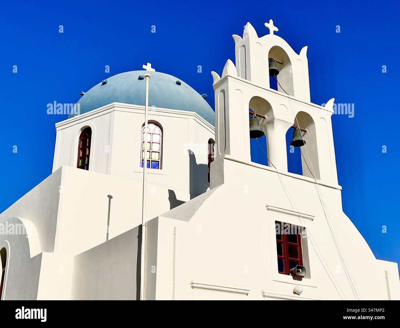 Whitewashed church with blue dome and bell tower against a bright blue summer sky in Oia, Santorini. - Smartphone Captured Stock Image