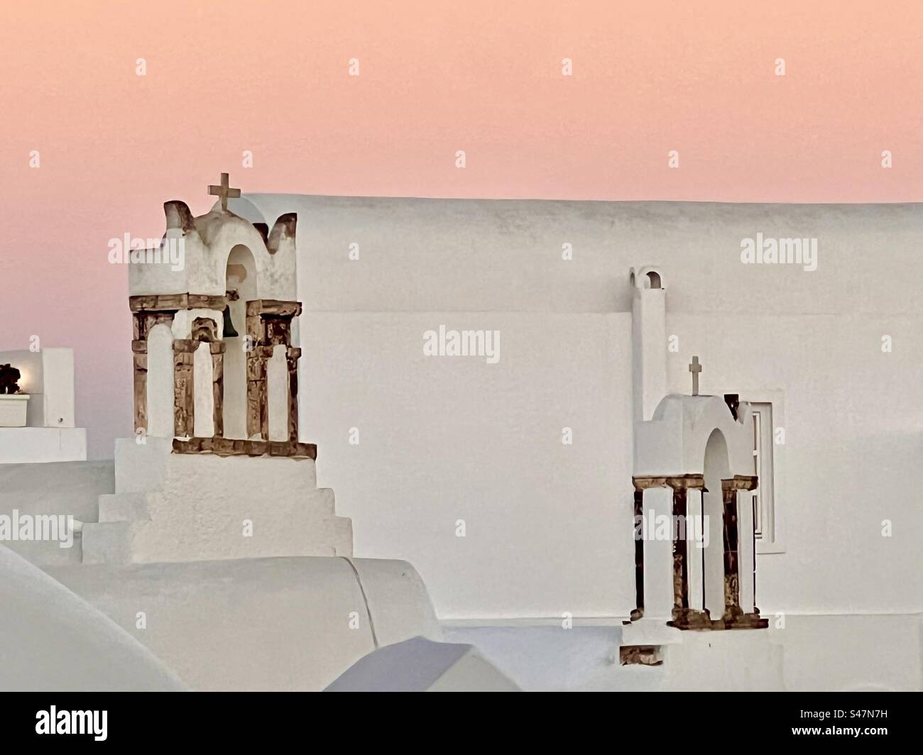 White bell towers with brown accents on a whitewashed structure in Oia, Santorini with the vibrant orange glowing sunset surrounding. - Smartphone Captured Stock Image