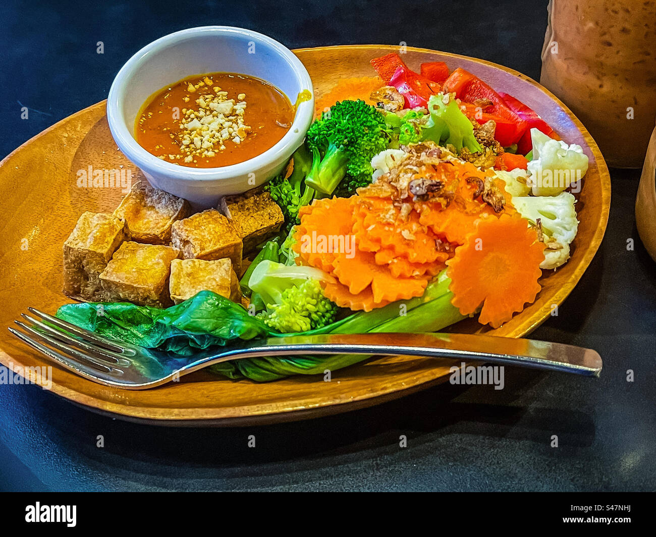 High angle view of crispy fried tofu cubes and freshly steamed vegetables with a spicy peanut sauce dip in bowl on plate on table. Vegetarian/vegan food. Healthy eating. Asian food. Eat your colors. - Smartphone Captured Stock Image