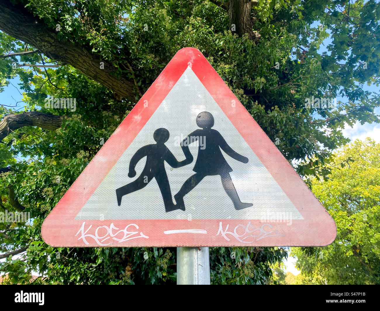 A triangle shaped road sign warning drivers about children crossing the road near a school. Stock Photo