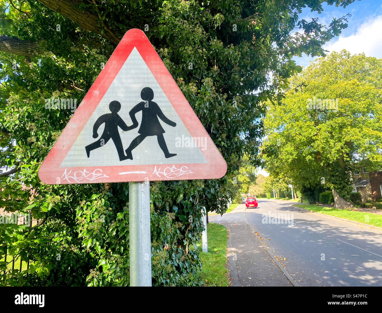 A triangle shaped road sign warning drivers about children crossing the road near a school. - Smartphone Captured Stock Image