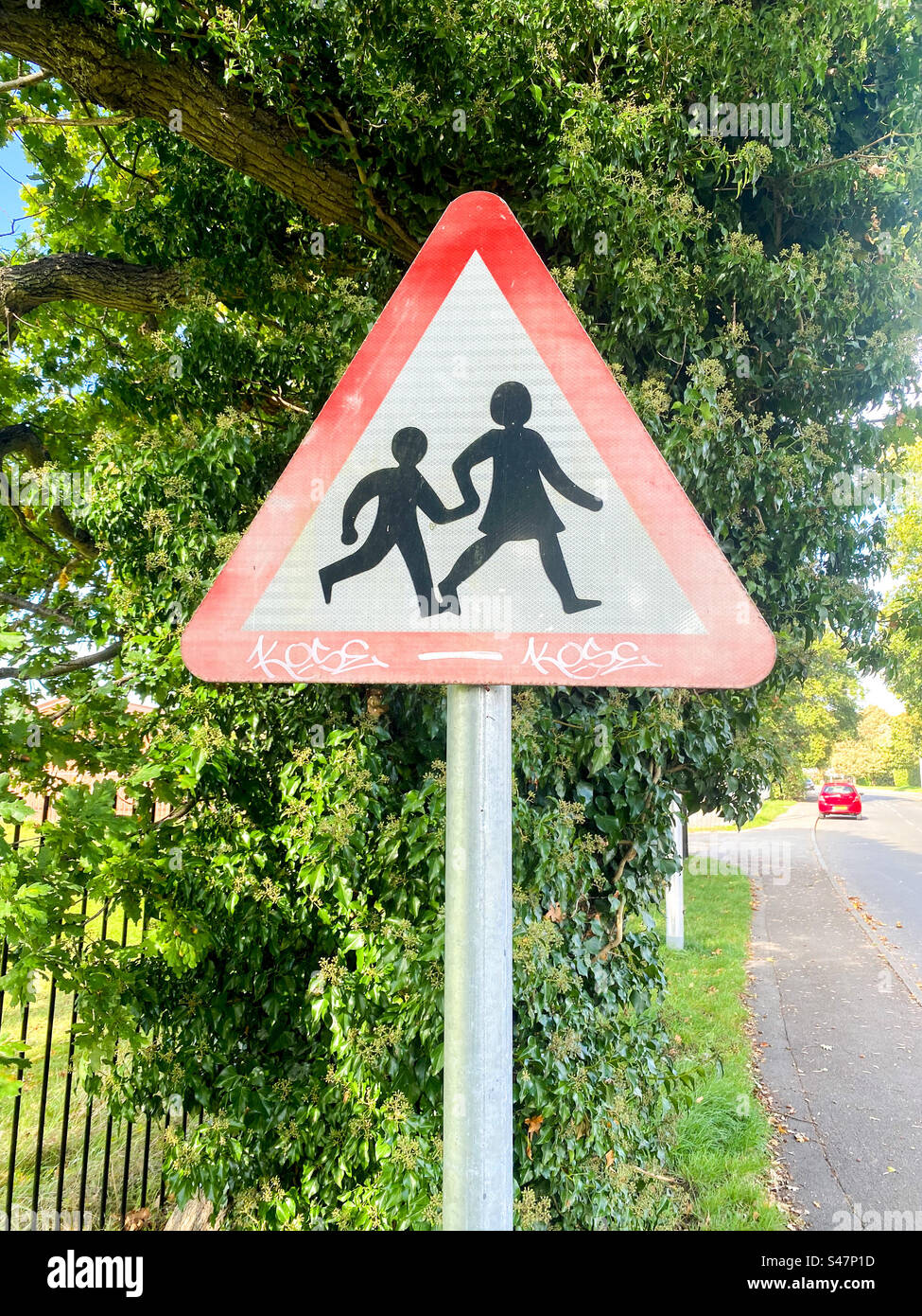 A triangle shaped road sign warning drivers about children crossing the road near a school. Stock Photo