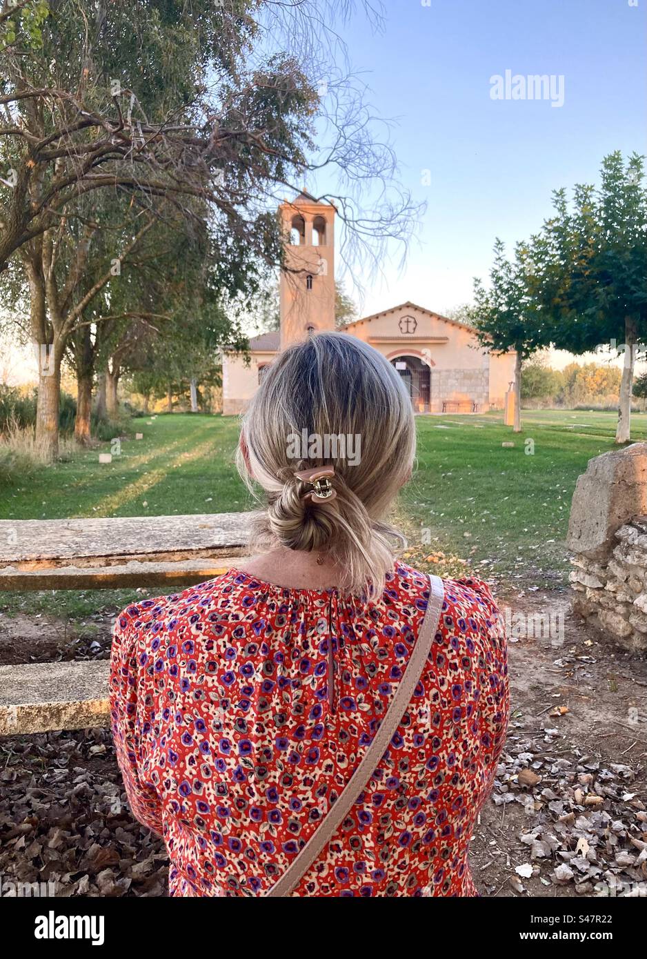 Back of the head of a blonde woman with tied up hair sitting looking towards the Ermita church Lantada Lantadilla Palencia Spain - Smartphone Captured Stock Image