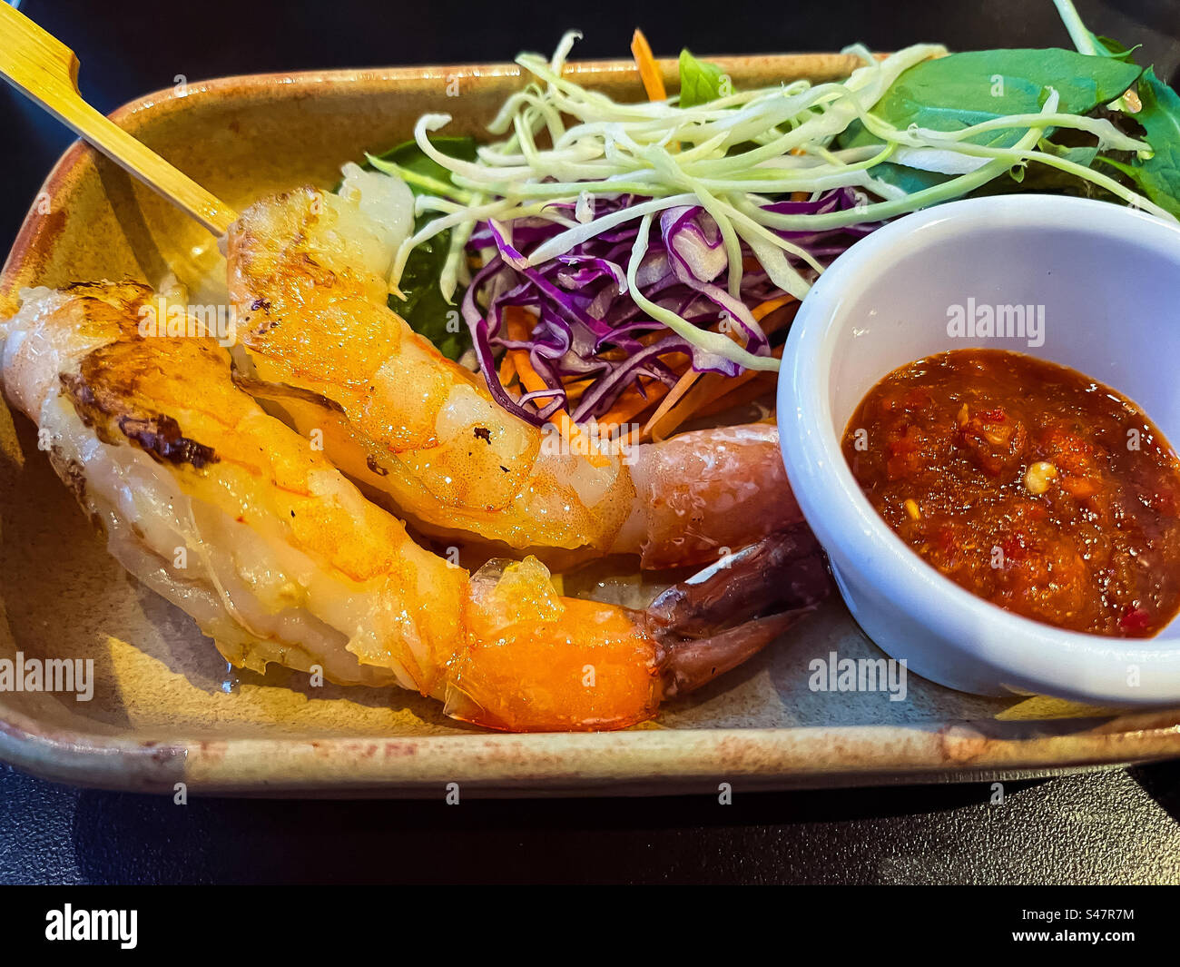 Close-up of grilled prawn skewers and fresh salad on plate with a bowl of spicy chili sauce on table. Healthy eating. Asian food. Spice. Sambal. - Smartphone Captured Stock Image