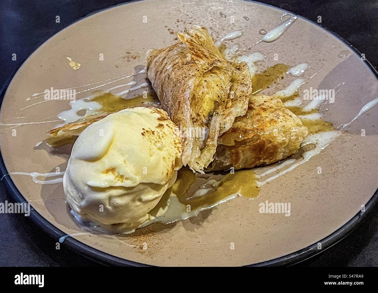 High angle, close-up view of banana fritters with syrup and a scoop of vanilla ice-cream on plate on table. Dessert. Sweet food. - Smartphone Captured Stock Image