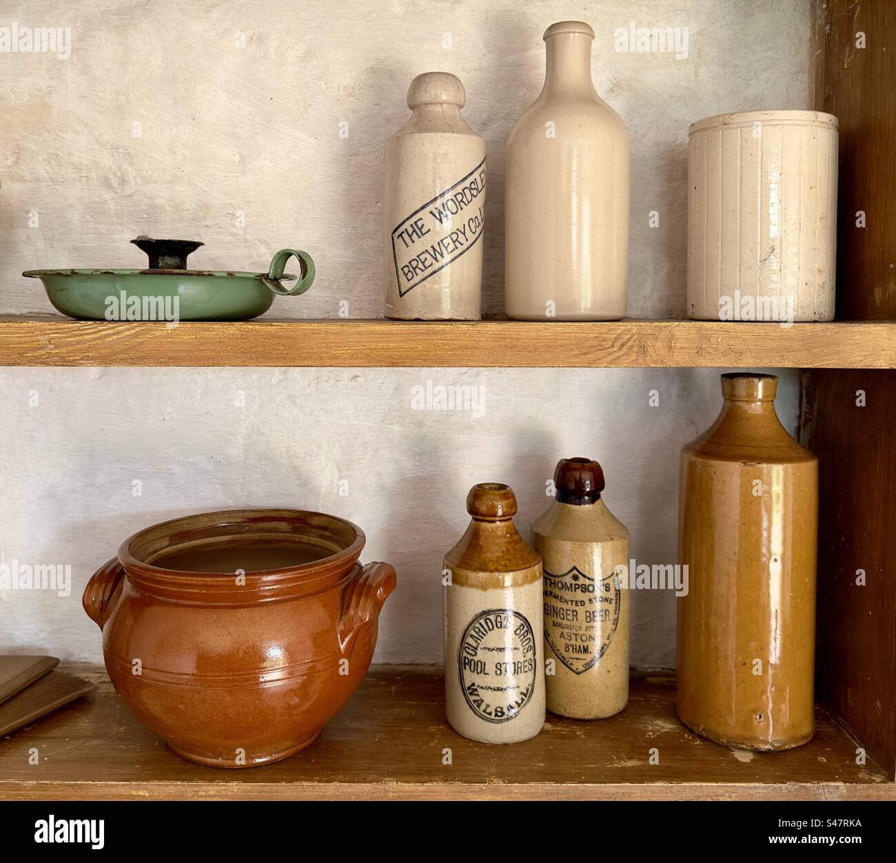 Wooden shelves in a museum setting with a row of assorted household objects, including ginger, beer bottles, and a stew pot Stock Photo