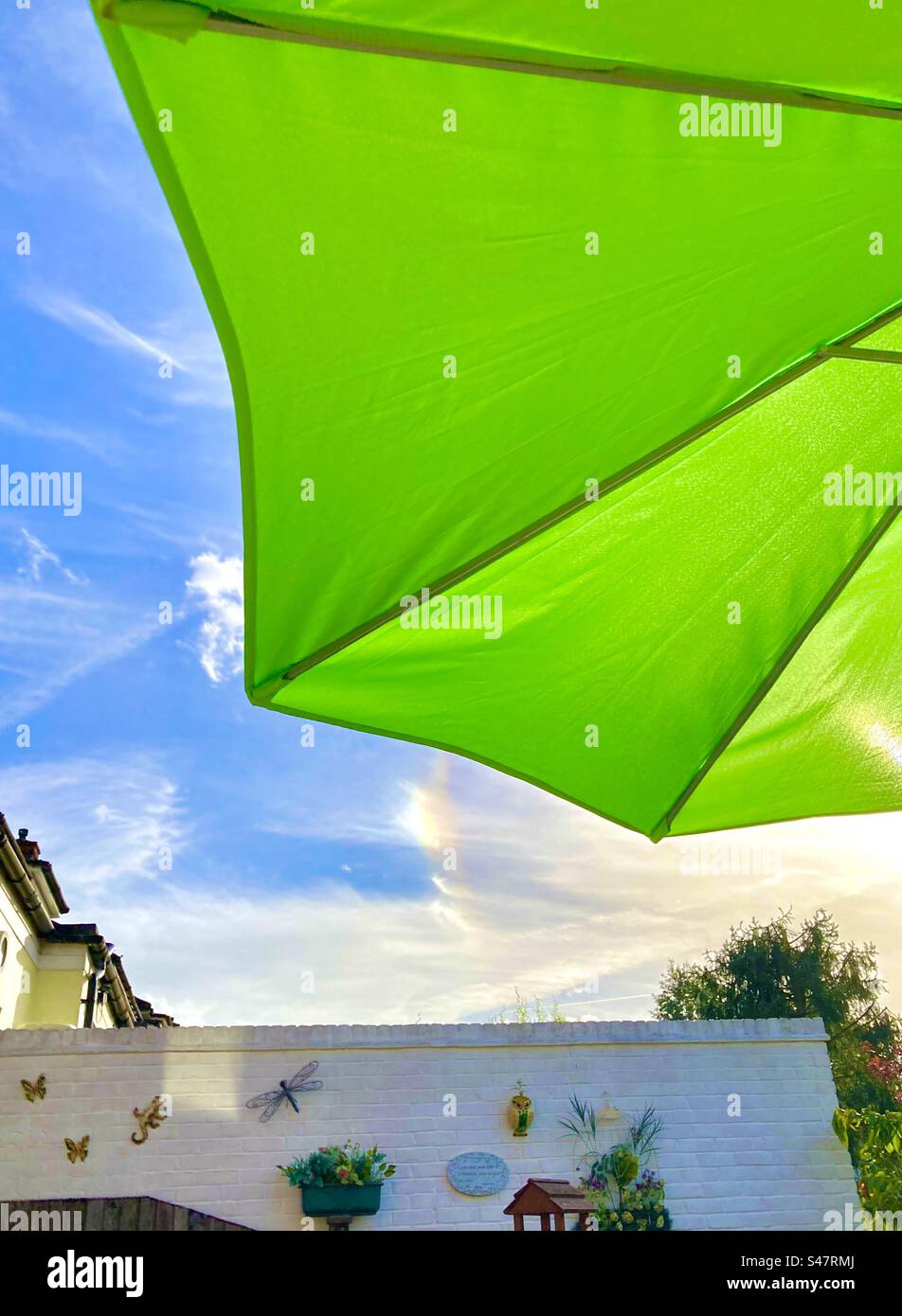 Bright green garden parasol on a hot sunny afternoon with a partial rainbow in an English garden - Smartphone Captured Stock Image