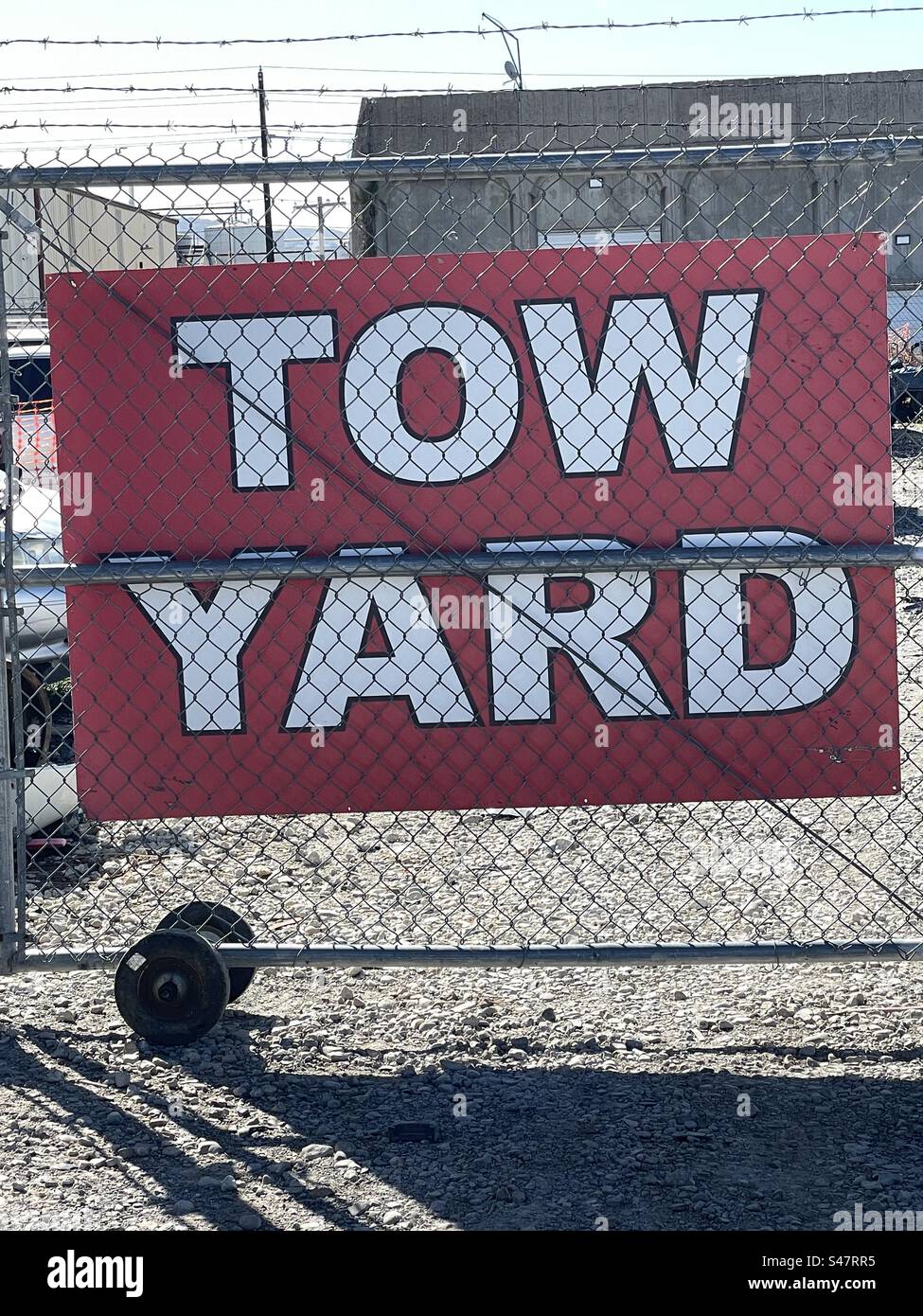 Tow yard gate and a barbed wire fence with signage identifying this storage lot as a tow yard. - Smartphone Captured Stock Image