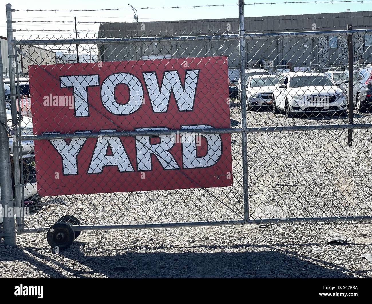 Tow yard gate and a barbed wire fence with signage identifying this storage lot as a tow yard. - Smartphone Captured Stock Image
