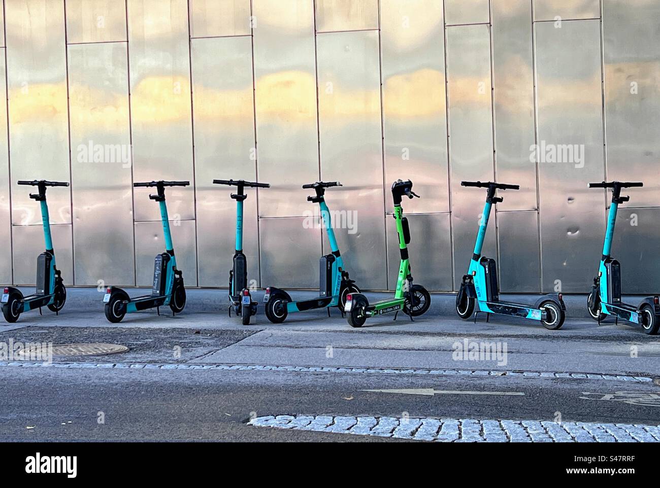 Tier city e-scooters parked in a row on the street walkway next to the shiny metal element building wall - Smartphone Captured Stock Image