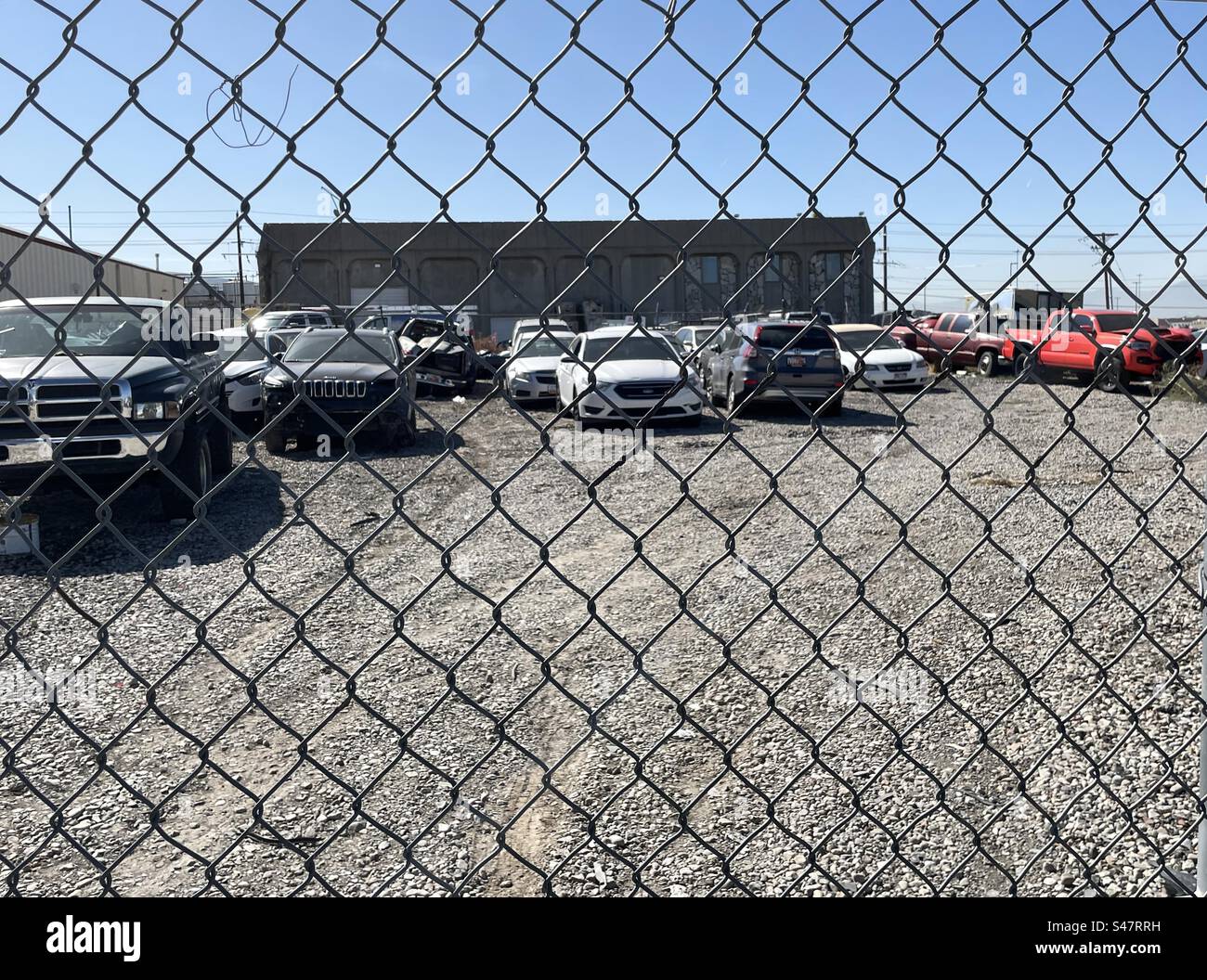 Tow yard, with a surrounding barbed wire chain link fence, to keep cars safe that have been wrecked and damaged. Stock Photo
