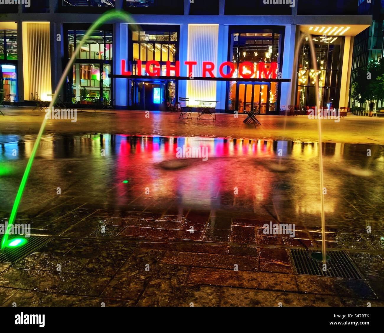 Two jets of water in the public square, Coal Drop Yard in Kings Cross in London illuminated with neon lights at night. Stock Photo