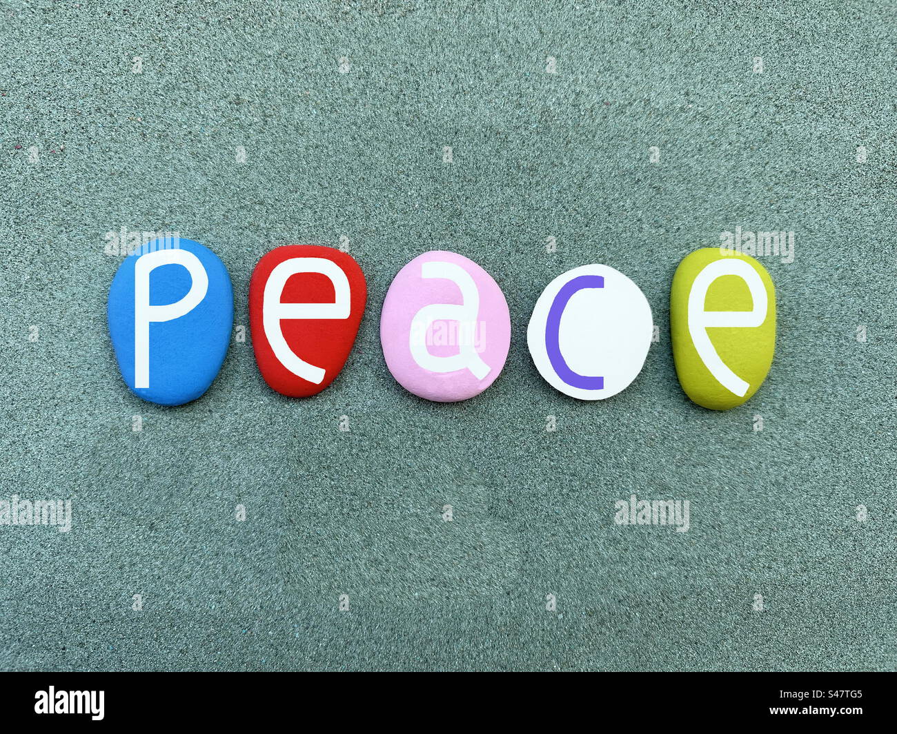 Peace word composed with multi colored hand painted stone letters over green sand - Smartphone Captured Stock Image