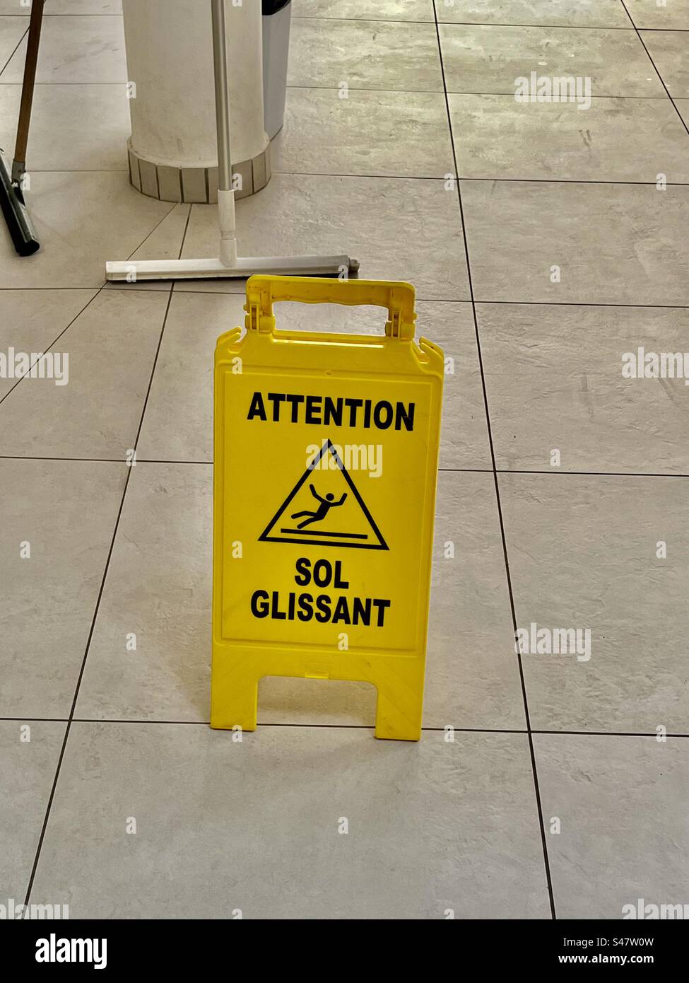 Wet floor sign French attention sol glissant slippery surface person slipping over fall falling pool wet water environment shower bathroom yellow signage squeegee sweeper France Stock Photo