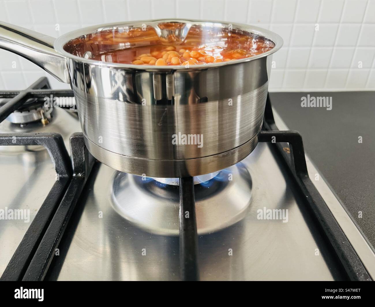 Baked beans being cooked in a stainless steel pan on a gas hob Stock
