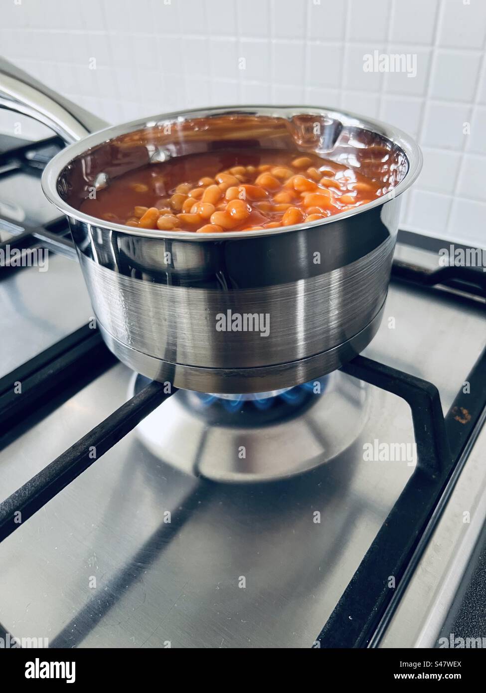 Baked beans in a stainless steel pan being cooked on a gas hob Stock