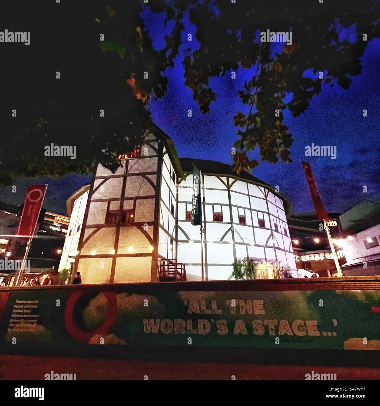 Banner with Shakespeare quote “All the World’s a Stage” and the Globe Theatre illuminated at night in London - the Globe Theatre is a replica of theatre in William Shakespeare’s time - Smartphone Captured Stock Image