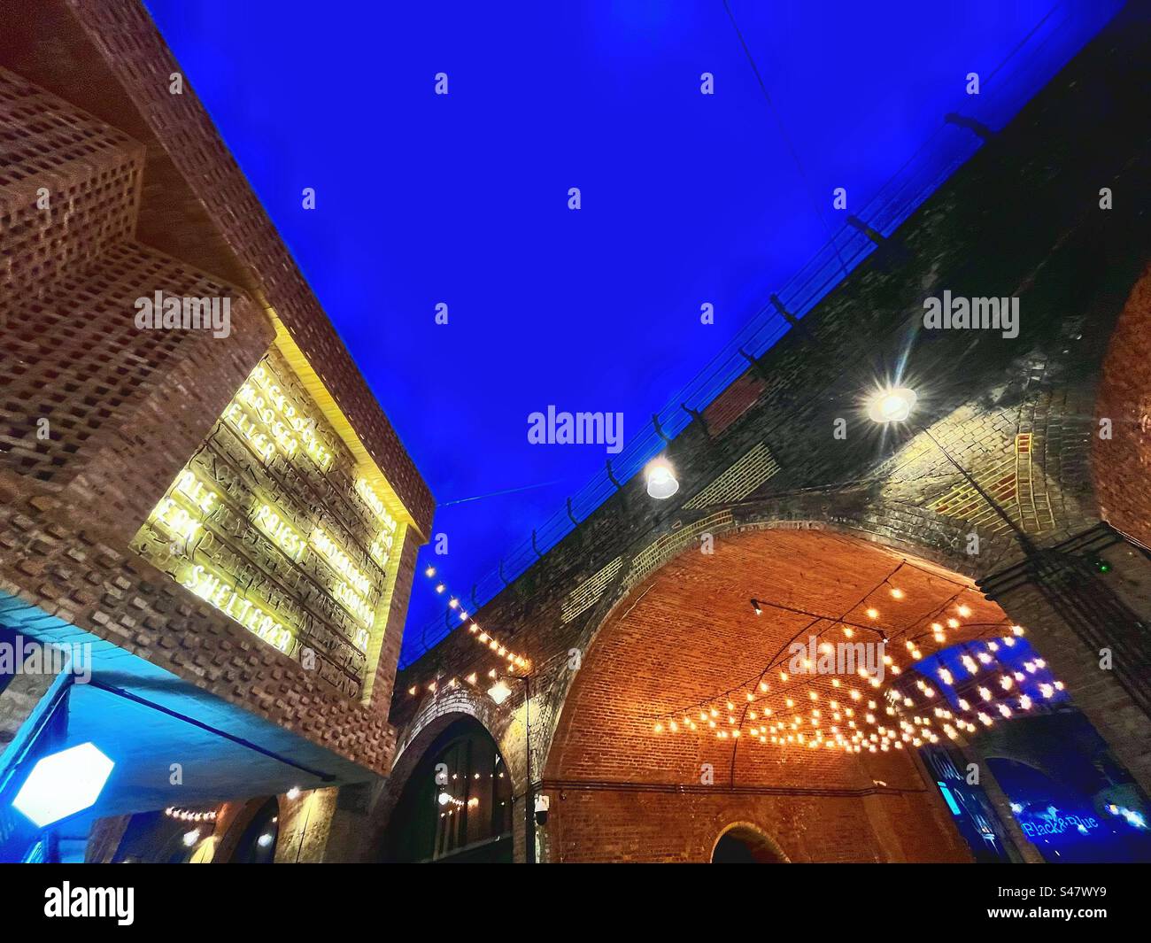 Borough Market is under the railway tracks in London - railways have shaped London since the Victorian times. Night Photography with lights and arch and notices - Smartphone Captured Stock Image