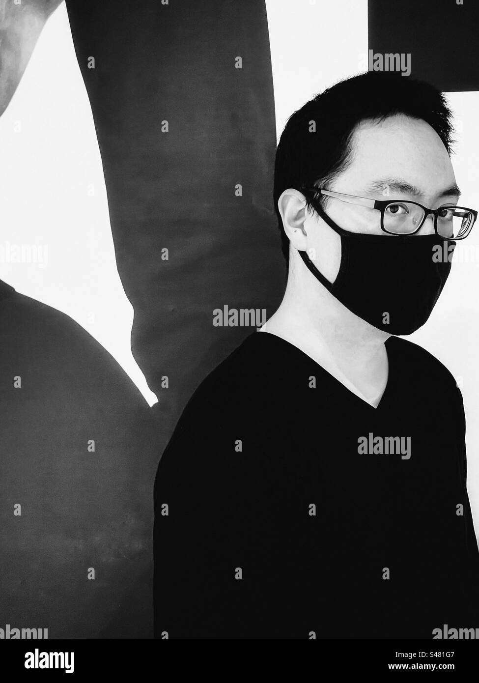 Monochrome shot of young Asian man in eyeglasses and face mask standing against geometric patterned background, from the waist up. Vision care. Pattern. Line. - Smartphone Captured Stock Image