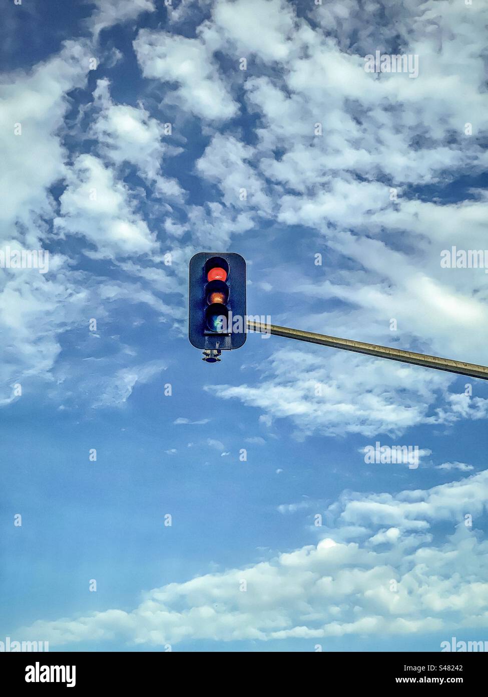 Low angle view of red stoplight showing at a traffic light against blue sky with white clouds. - Smartphone Captured Stock Image