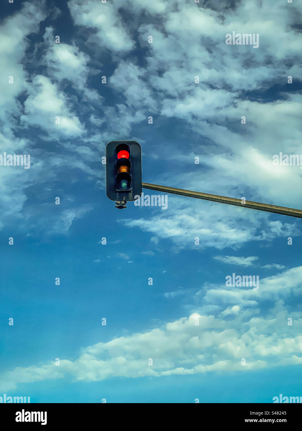 Low angle view of red stoplight showing at a traffic light against blue sky with white clouds. - Smartphone Captured Stock Image