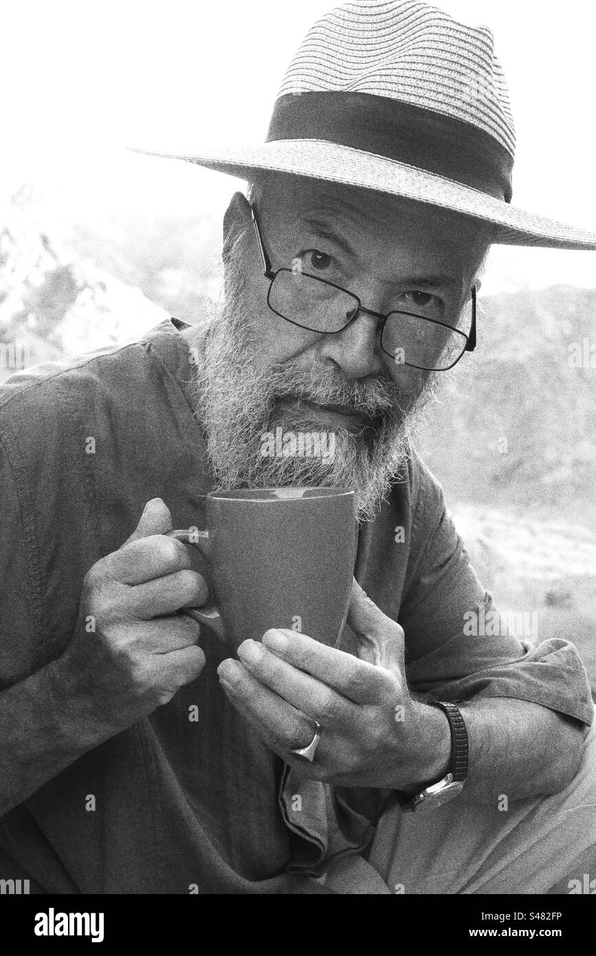Monochrome Portrait of senior man drinking coffee against mountains Stock Photo