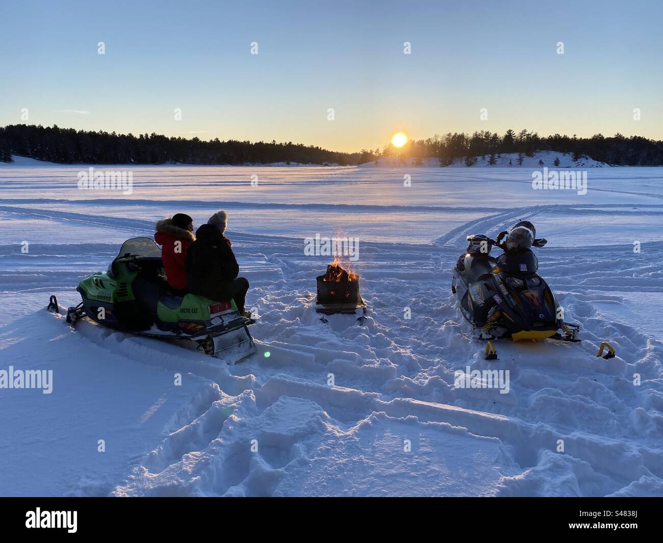 Sitting on snowmobiles by a fire on a frozen lake at sunset, parry sound Canada. Stock Photo