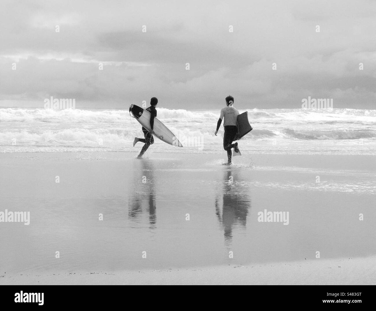 A surfer and a bodyboarder run towards the ocean. Carcavelos, Portugal. - Smartphone Captured Stock Image