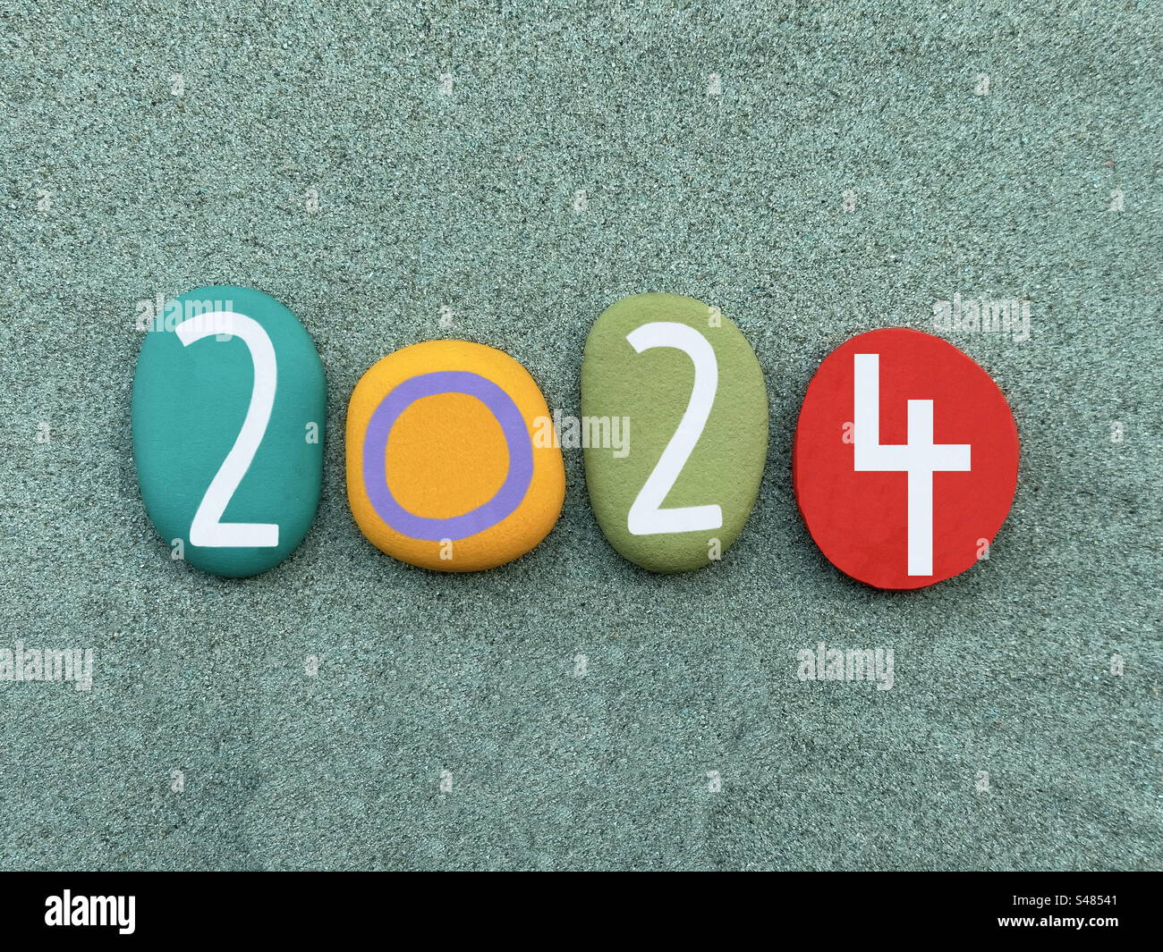 Year 2024 celebrated with hand painted multi colored stone numbers over green sand - Smartphone Captured Stock Image