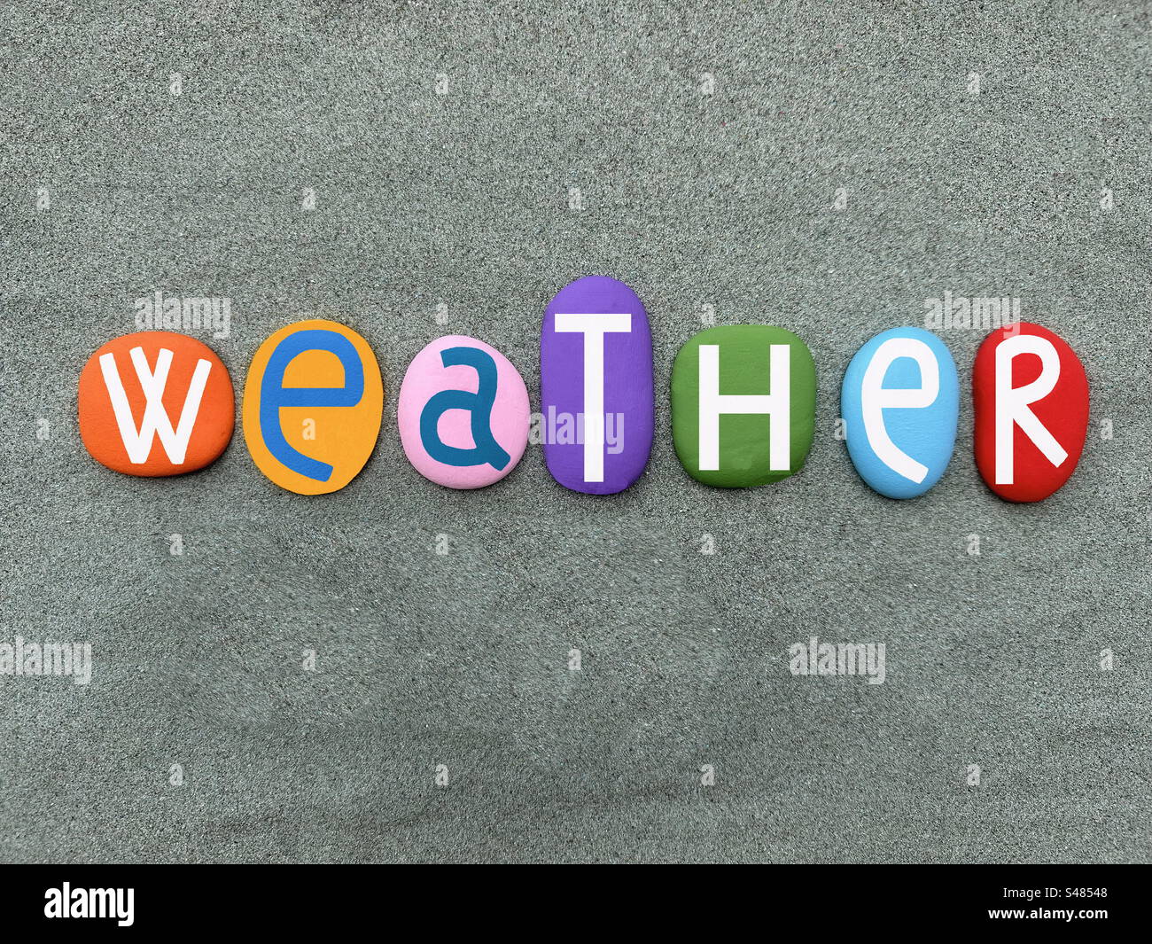 Weather word composed with hand painted multi colored stone letters over green sand - Smartphone Captured Stock Image
