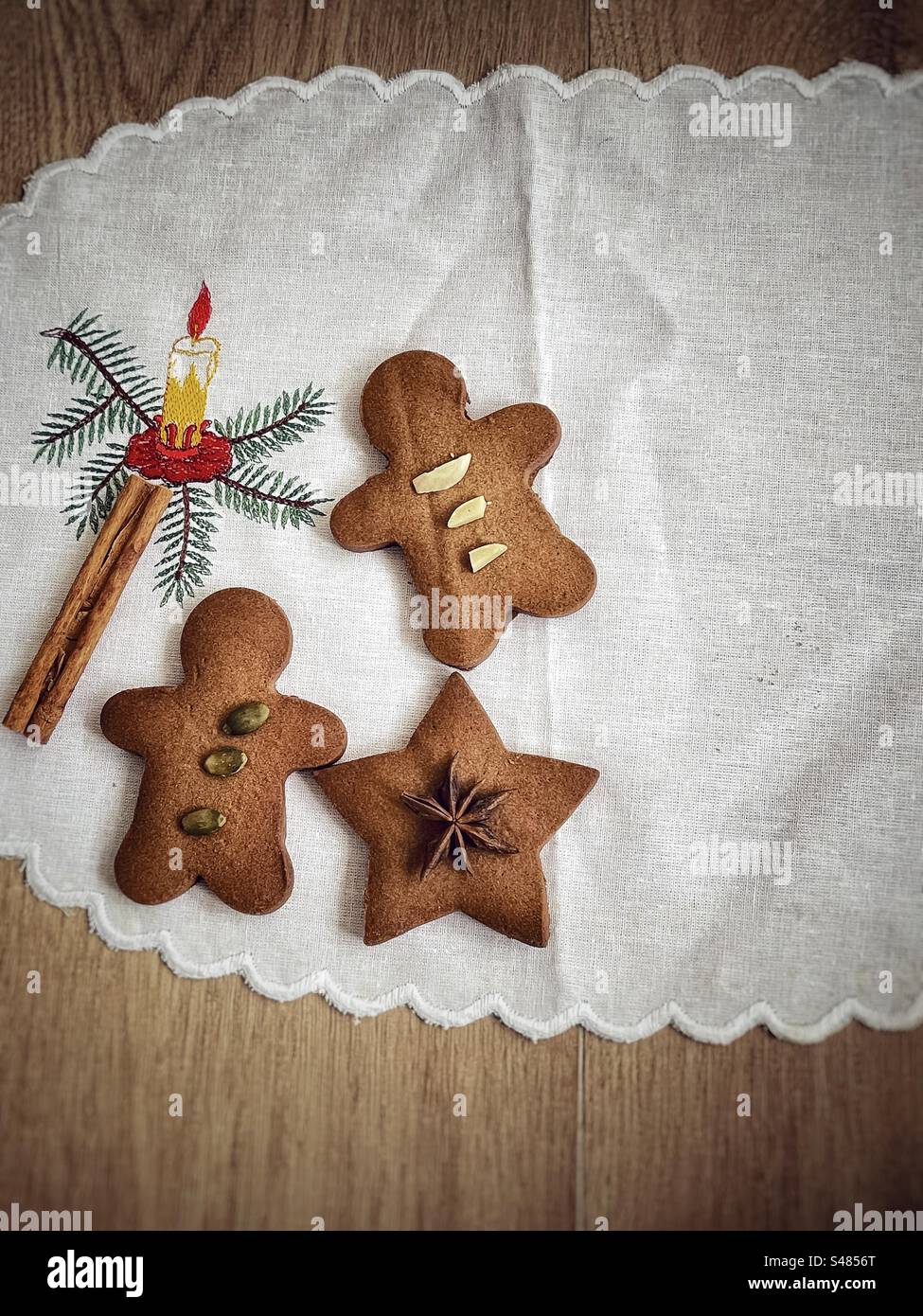 Vintage style Christmas concept with copy space. Flat lay of gingerbread cookies with nuts, seeds and spices on white tablecloth with embroidered Christmas candle. Still life. Gingerbread man and star - Smartphone Captured Stock Image