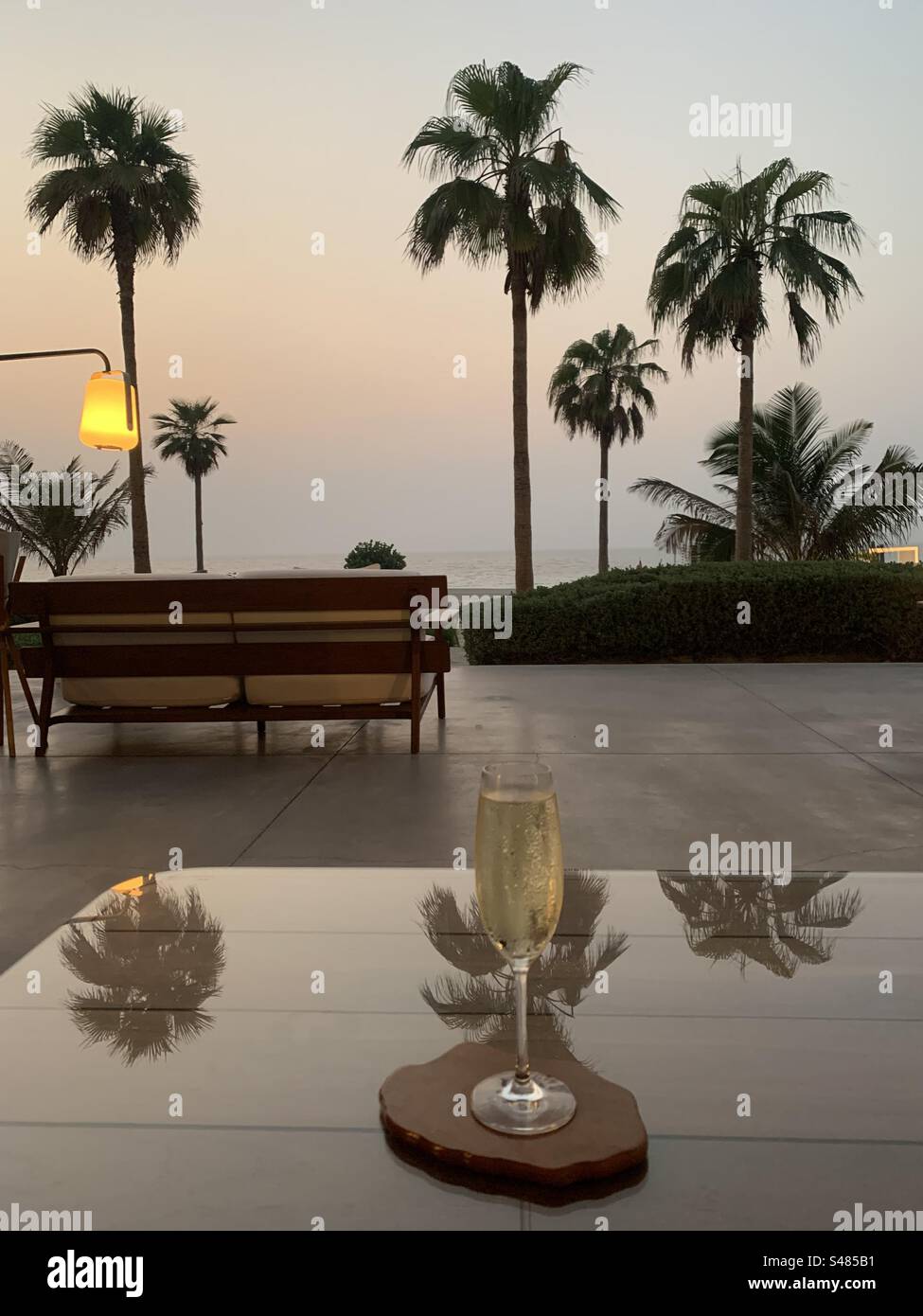 A glass of Prosecco on a terrace overlooking the beach at sunset - Smartphone Captured Stock Image