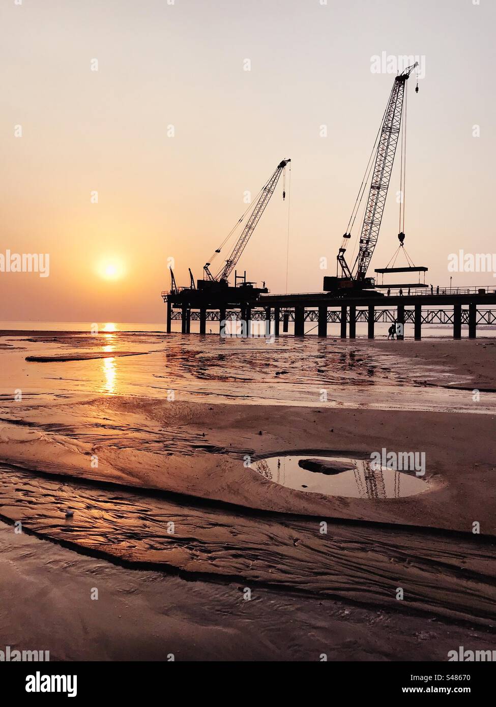 Cranes and heavy construction on a beach against the setting sun - Smartphone Captured Stock Image