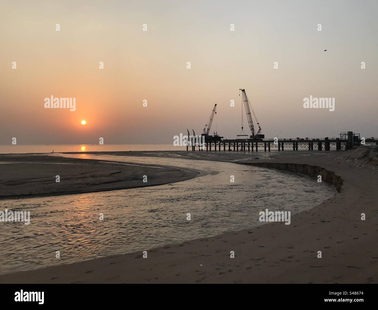 Cranes and heavy construction on a beach against the setting sun - Smartphone Captured Stock Image