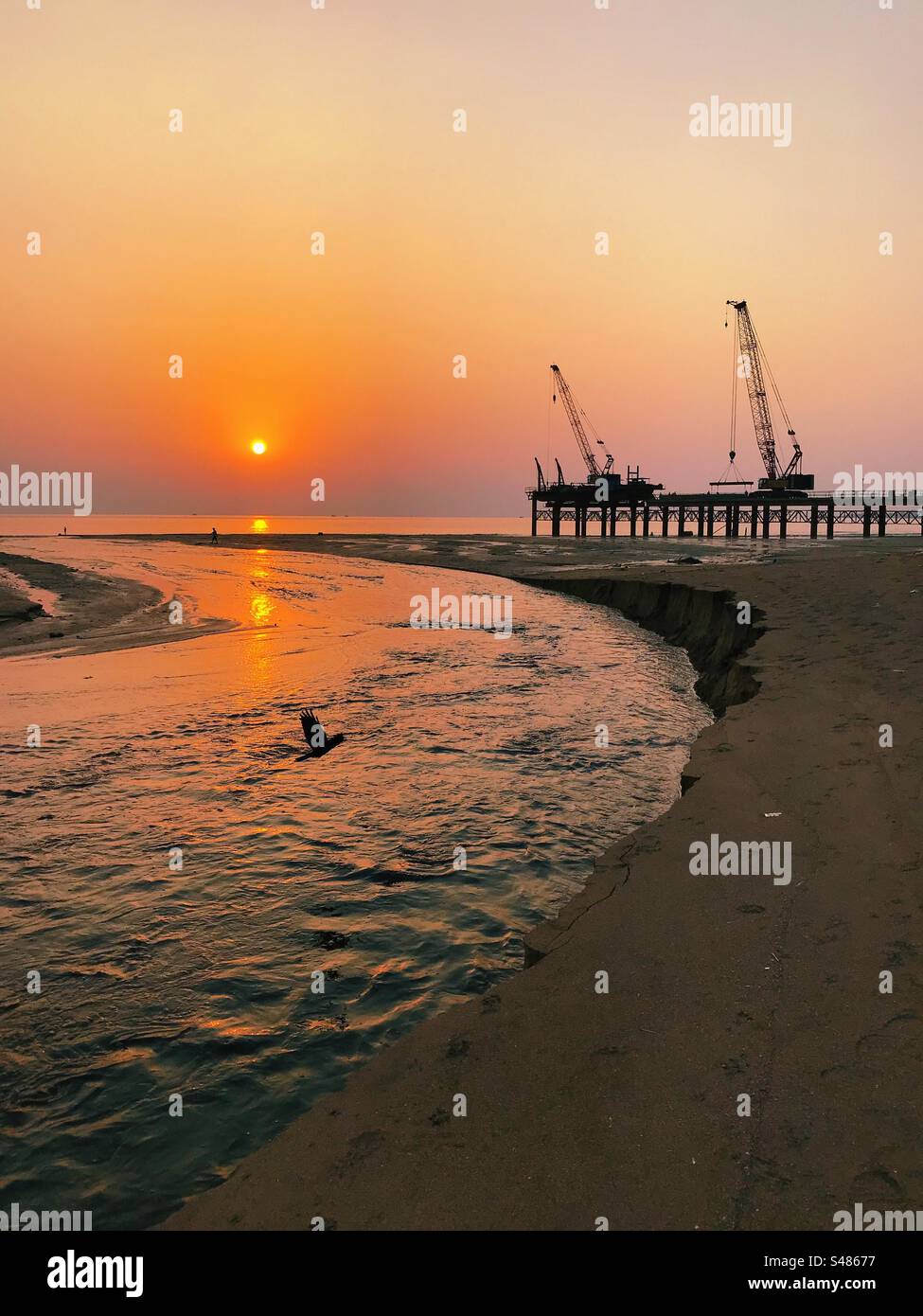Cranes and heavy construction on a beach against the setting sun - Smartphone Captured Stock Image