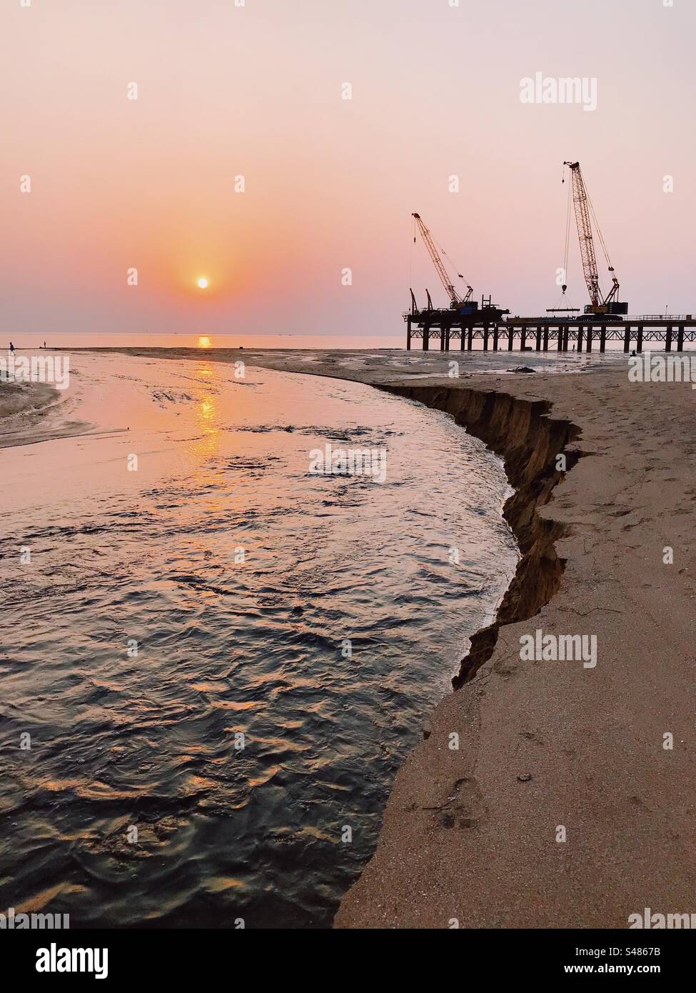 Cranes and heavy construction on a beach against the setting sun - Smartphone Captured Stock Image
