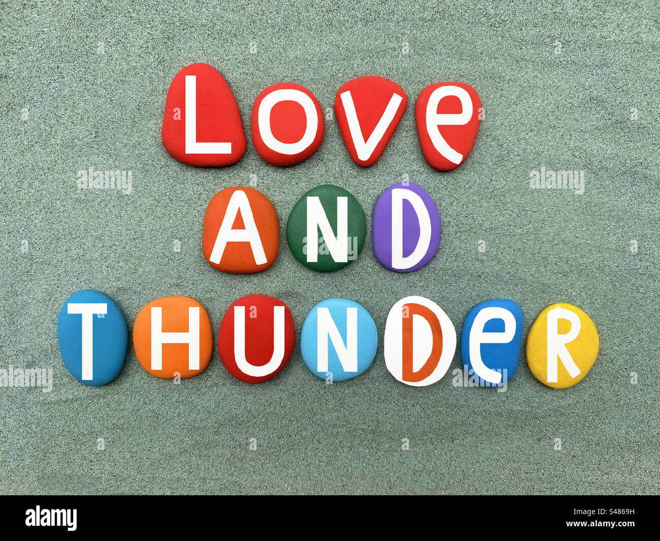Love and thunder, creative text composed with multi colored stone letters over green sand Stock Photo