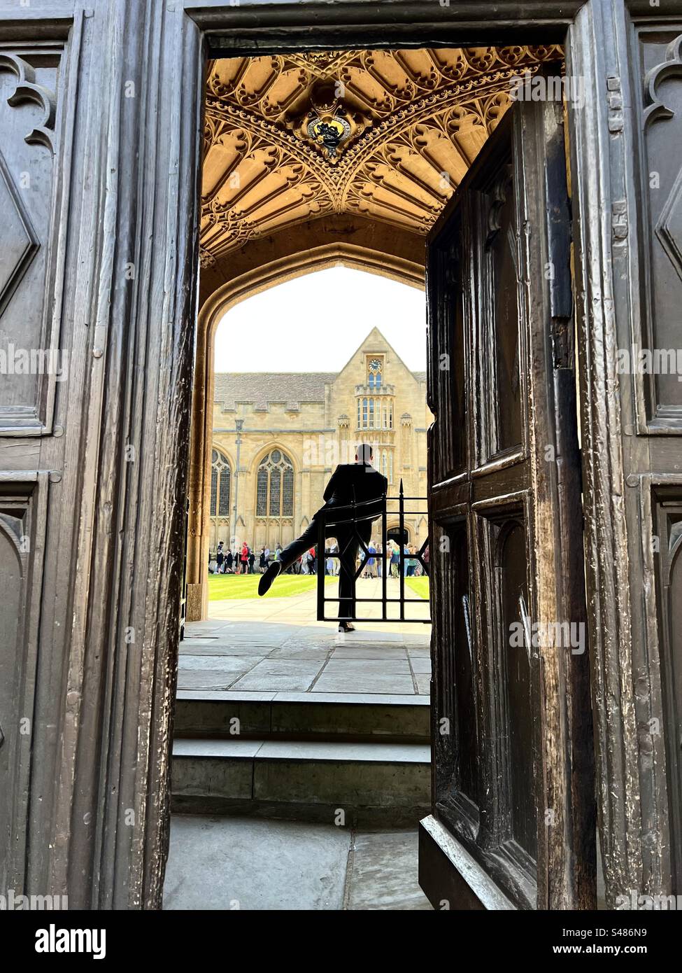 Man posing strangely at University College Oxford with a tourist party in the background Stock Photo