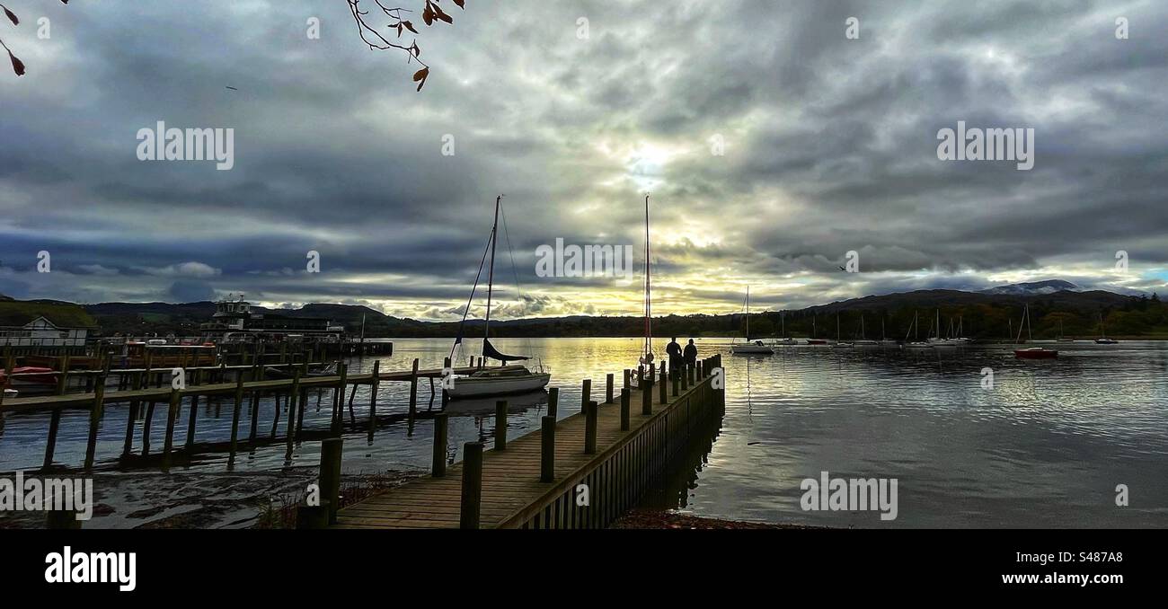 Looking over Windermere at dusk from Waterhead, Ambleside with a couple of people standing on the jetty - Lake District U.K. Stock Photo