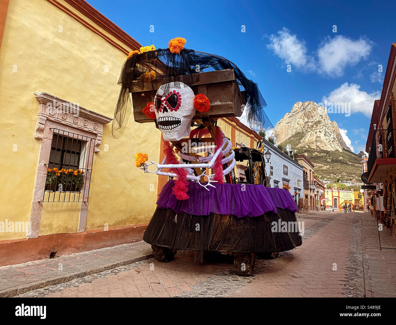 An excavator decorated as a catrina skeleton for halloween in front of the Peña de Bernal monolite mountain in San Sebastian Bernal, Queretaro, Mexico - Smartphone Captured Stock Image