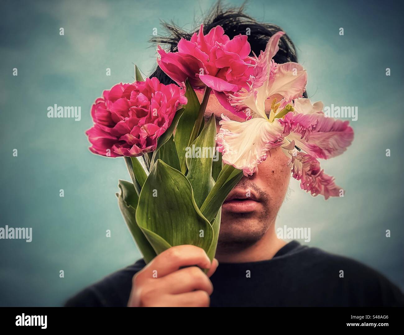 Close-up headshot of young man holding a bouquet of pink, double and parrot tulips against cloudy blue sky in springtime, vintage style. - Smartphone Captured Stock Image
