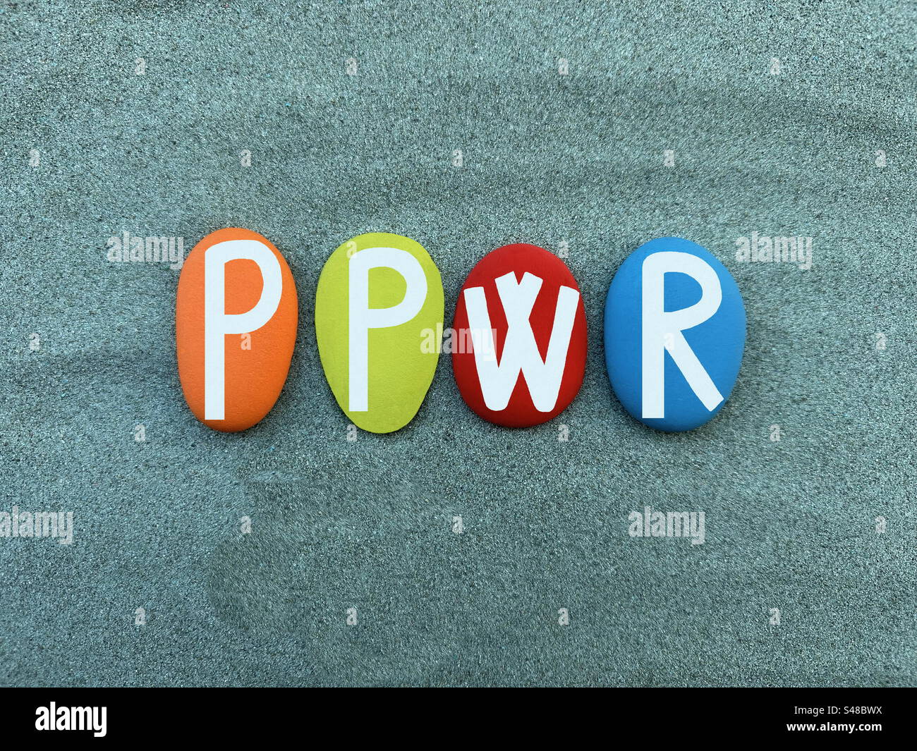 PPWR, Packaging and Packaging Waste Regulation composed with hand painted multi colored stone letters over green sand - Smartphone Captured Stock Image